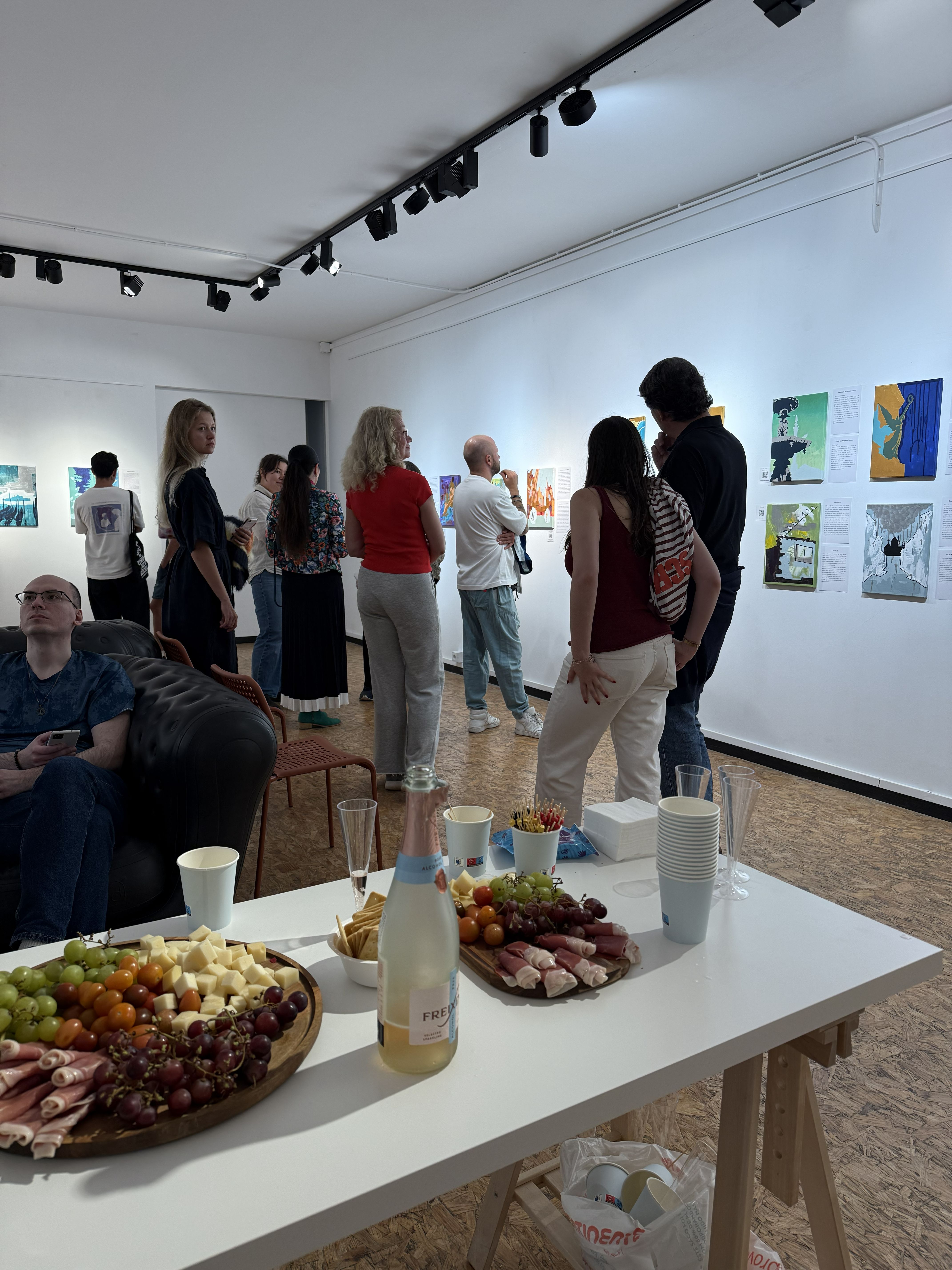 Many people in a big room with paintings and a table with food