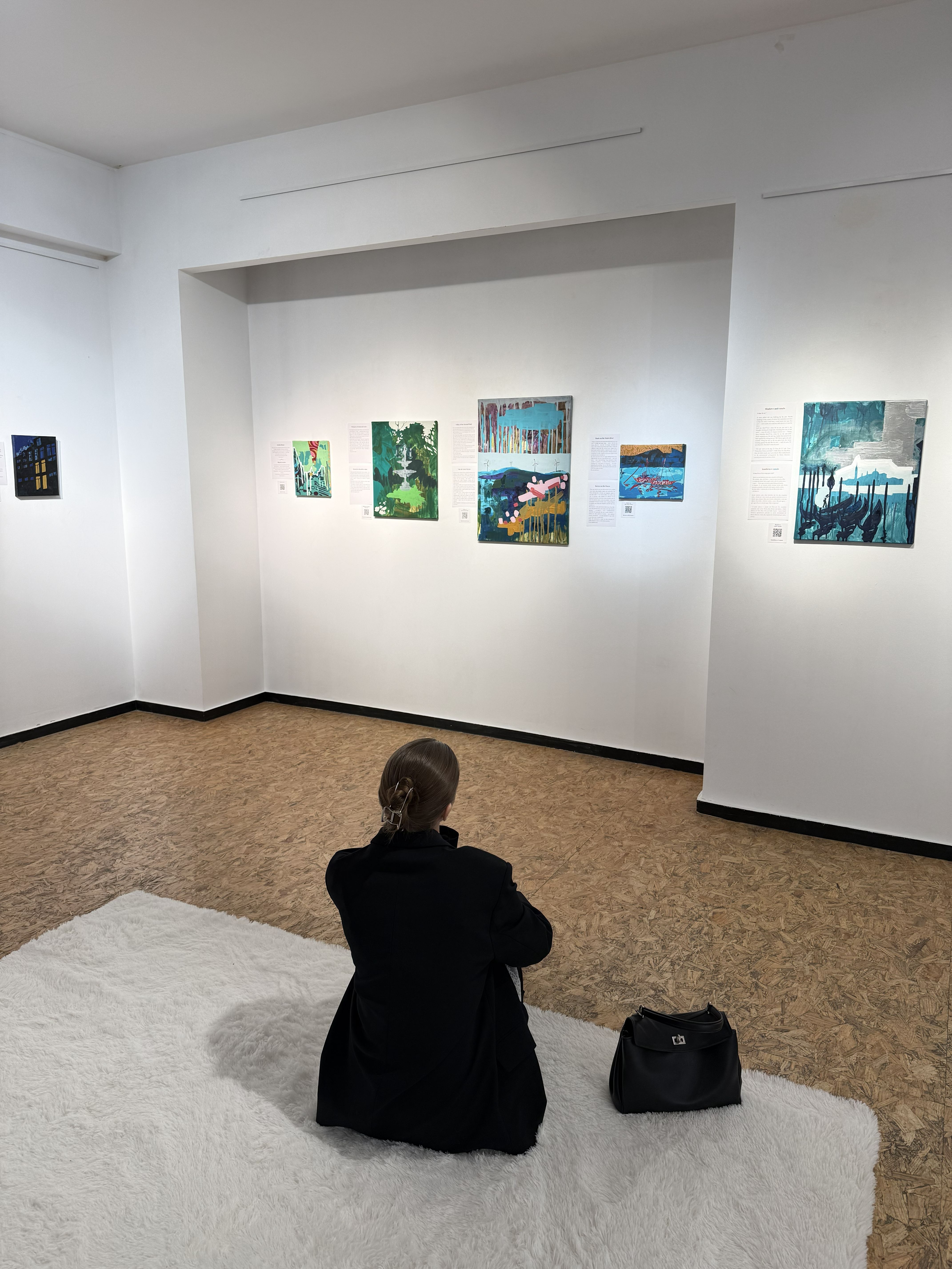 A person sitting on a white fluffy carpet and looking at the paintings on the wall