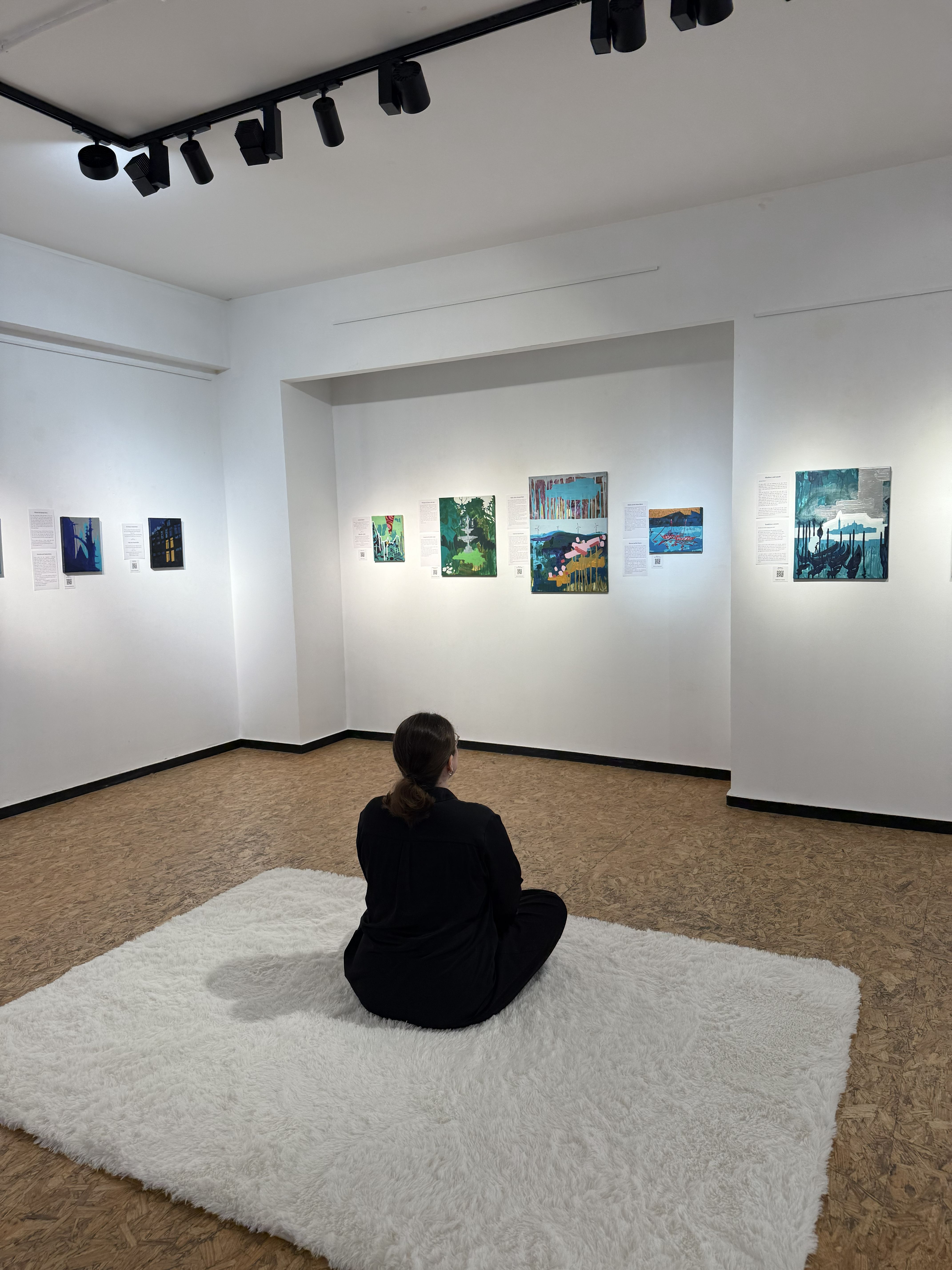Person sitting on a fluffy carpet in an exhibition room with paintings