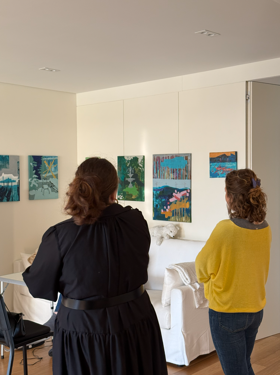 Two people looking at paintings on the walls in the well-lit room